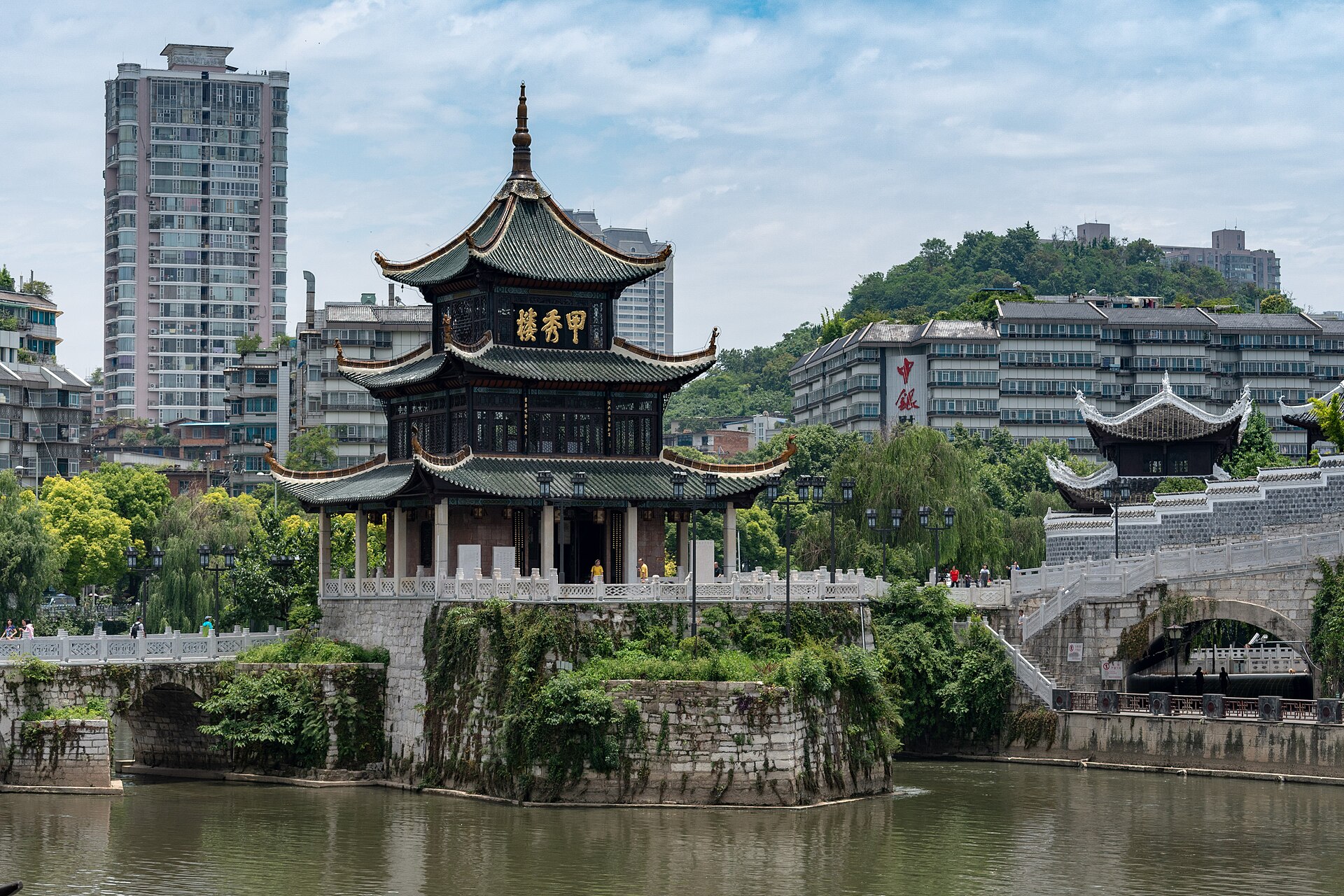 贵阳南明河畔的甲秀楼与浮玉桥,背后是城市建筑和绿树