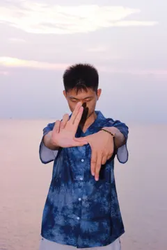 祖仁泽穿蓝色衬衫站在海边，天空呈柔和的晚霞色