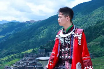外出旅行体验红色民族服装，侧身望向远处的山林