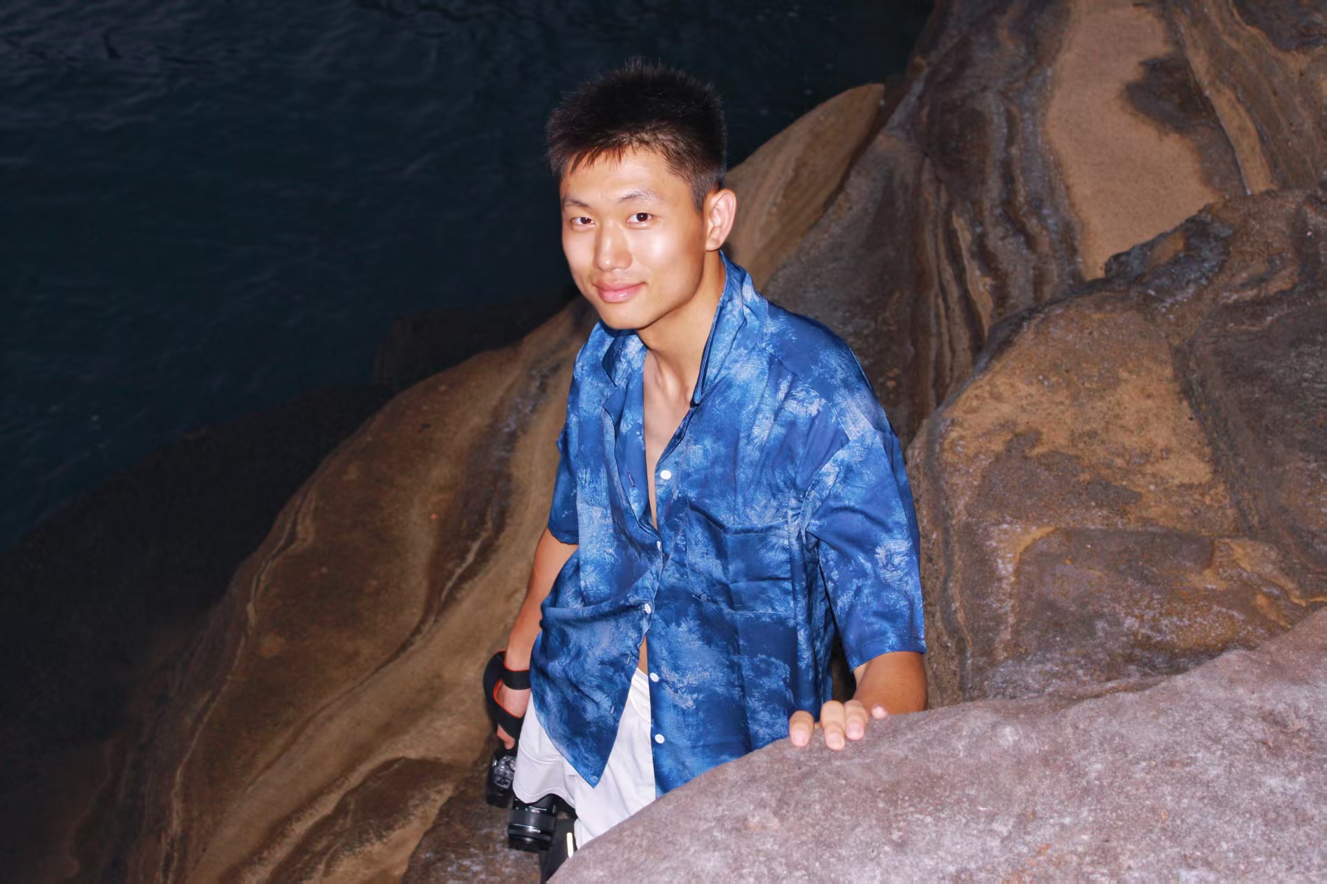 祖仁泽在海边的本人原照,身穿蓝衬衫,身后是岩石